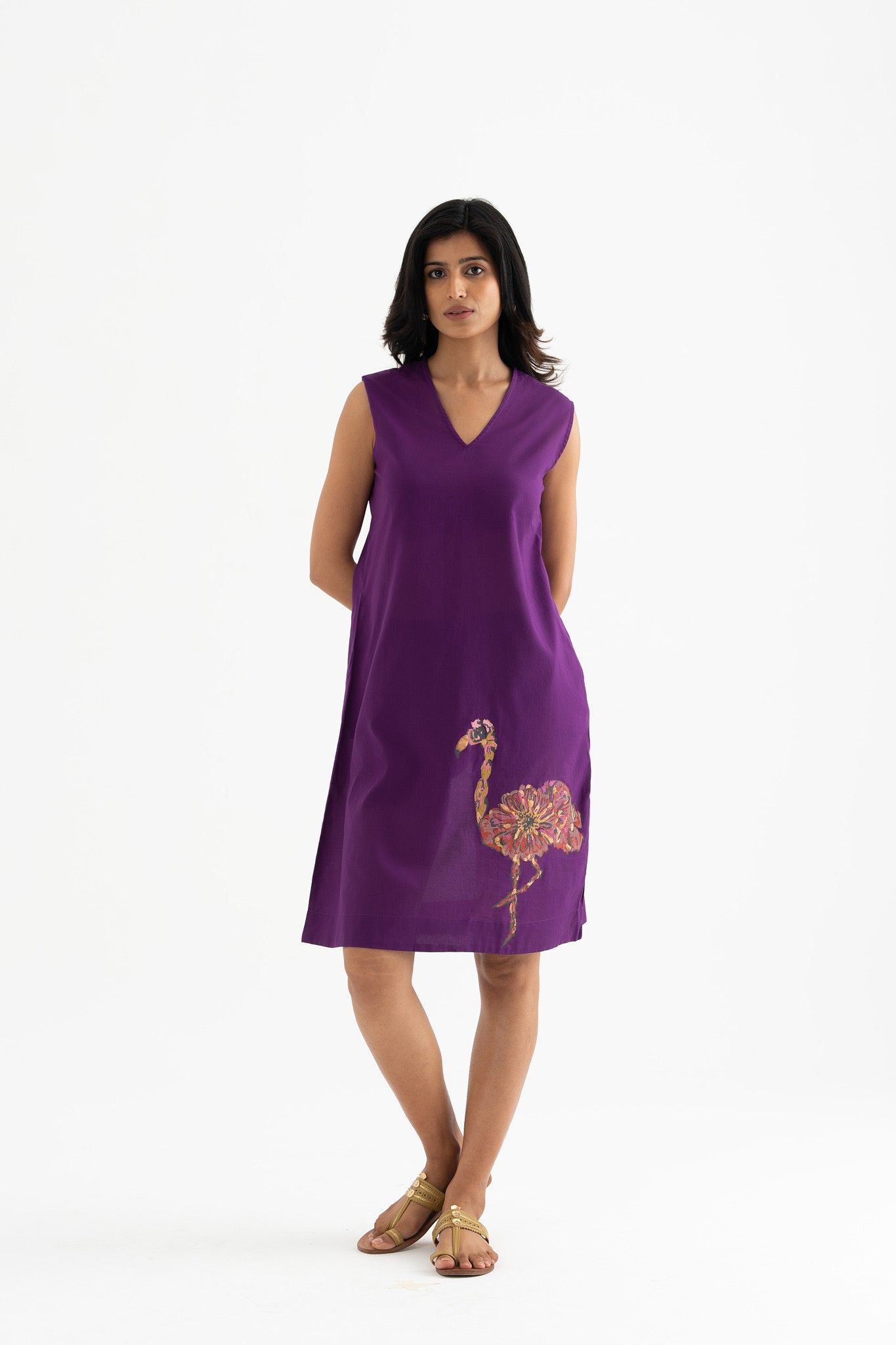 A woman standing and posing in a sleeveless, v-neck purple dress with a block-print flamingo on the front.