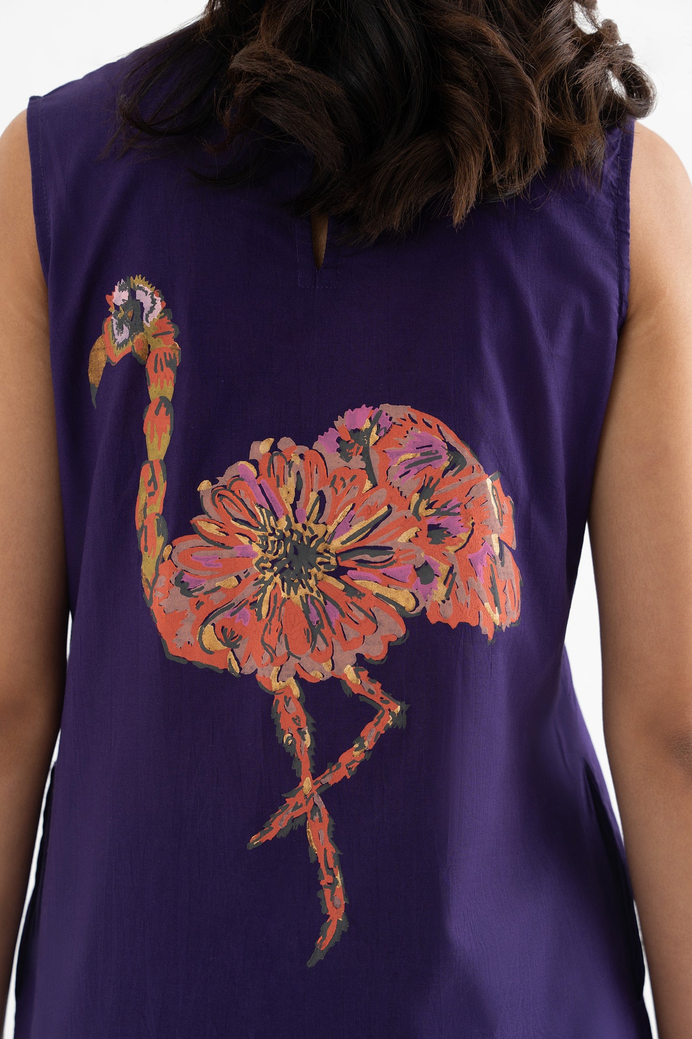 A woman wearing a sleeveless deep purple dress featuring a block-print flamingo pattern.
