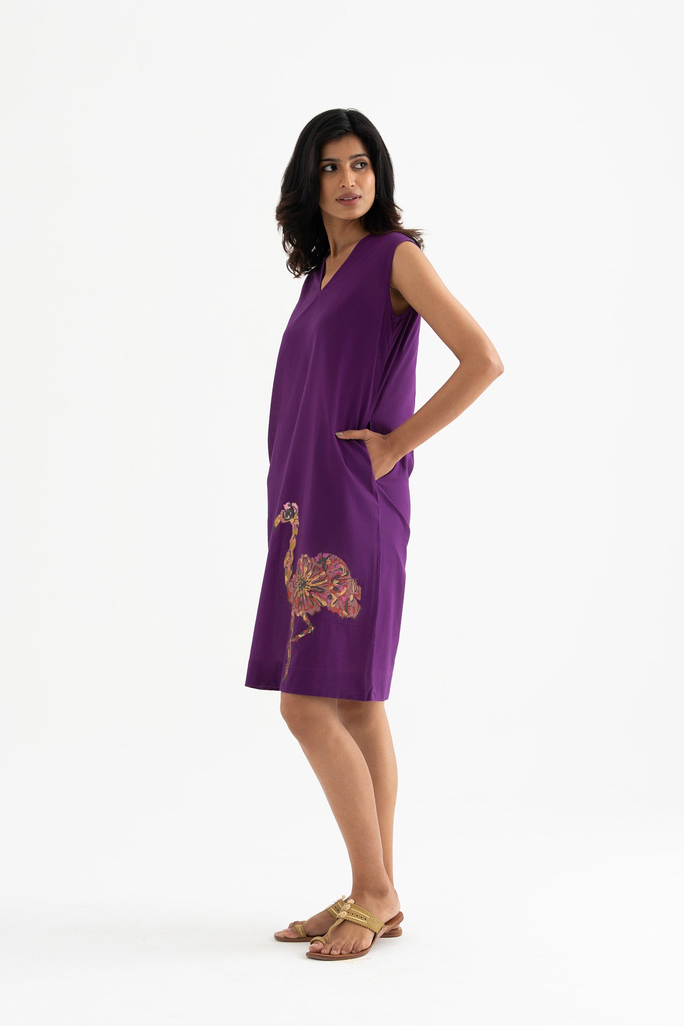 A woman standing and posing in a sleeveless, v-neck purple dress with a hand-printed flamingo on the front.