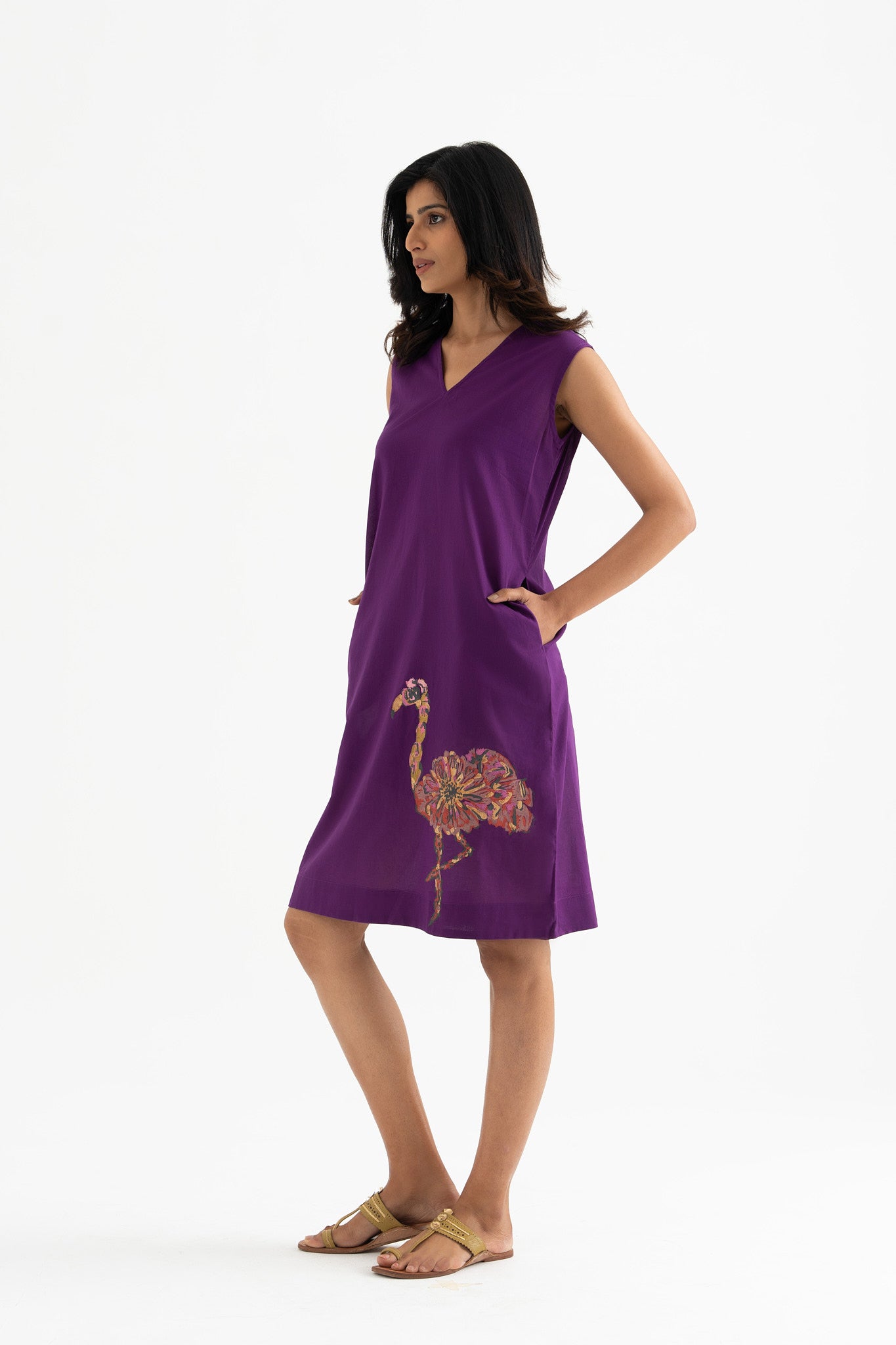 A woman standing and posing in a sleeveless, v-neck purple dress with a block-print flamingo on the front.