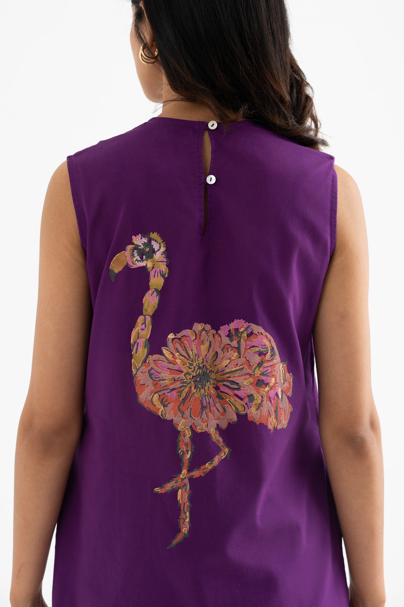 A woman in a sleeveless purple dress with a block-print flamingo on the back.